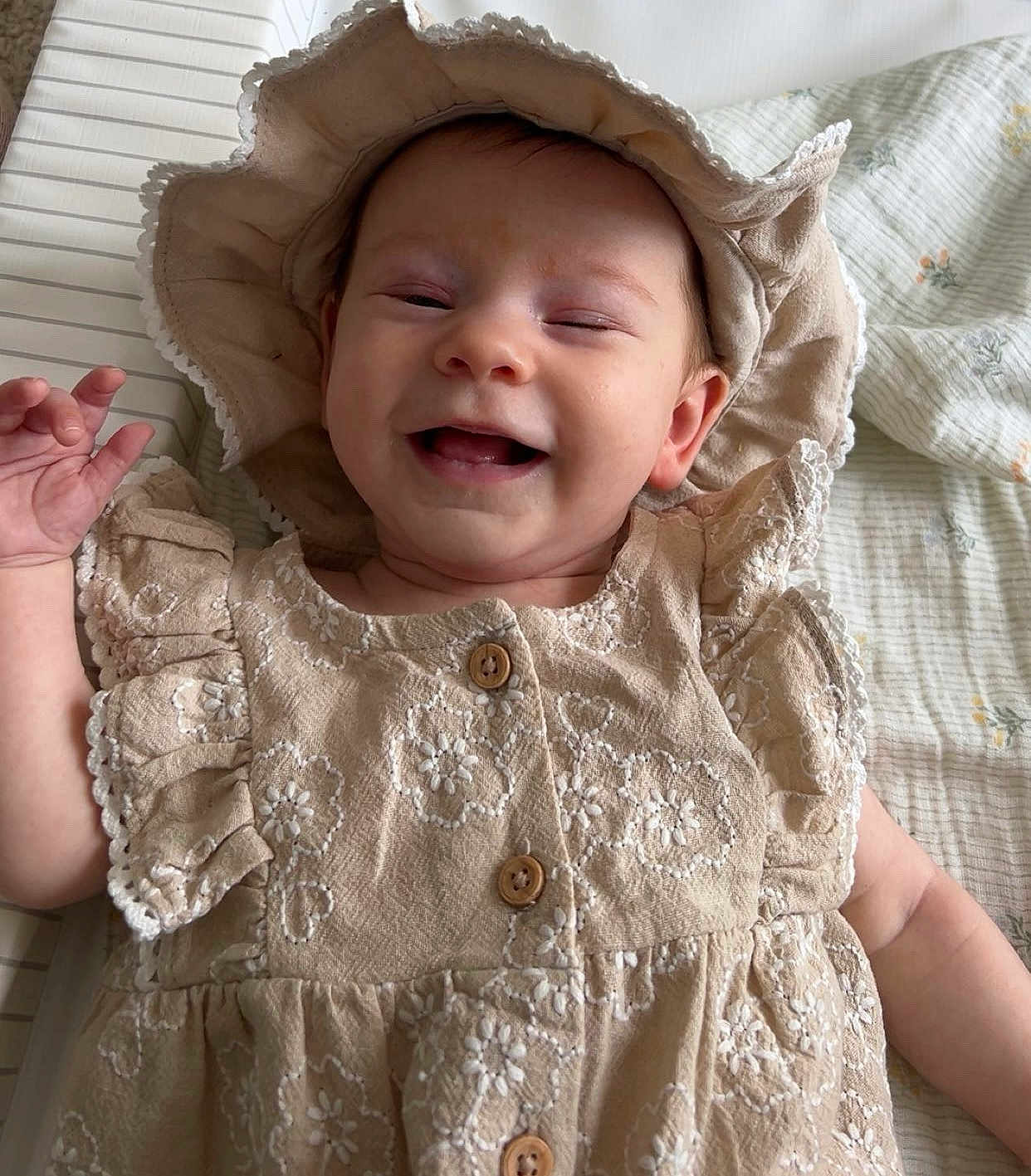 Lottie Mae joined the competition — help win amazing prizes! baby, child, smile, happy, hat, dress, beige, floral, pattern, button, hand, blanket, fabric, cute, infant, lying_down, portrait, clothing, person, indoors