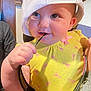 baby, child, cap, hat, yellow_clothing, sunglasses, hand, face, cheeks, pink_pattern, indoor, curious, mischievous, person, infant, cute, playful, closeup, portrait, holding