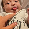Gracelynn joined the competition — help win amazing prizes! baby, child, close_up, clothing, cute, expression, face, finger, hand, indoors, infant, lying_down, person, playful, poking, shirt, skin, text_on_clothing, tongue_out, white_blanket