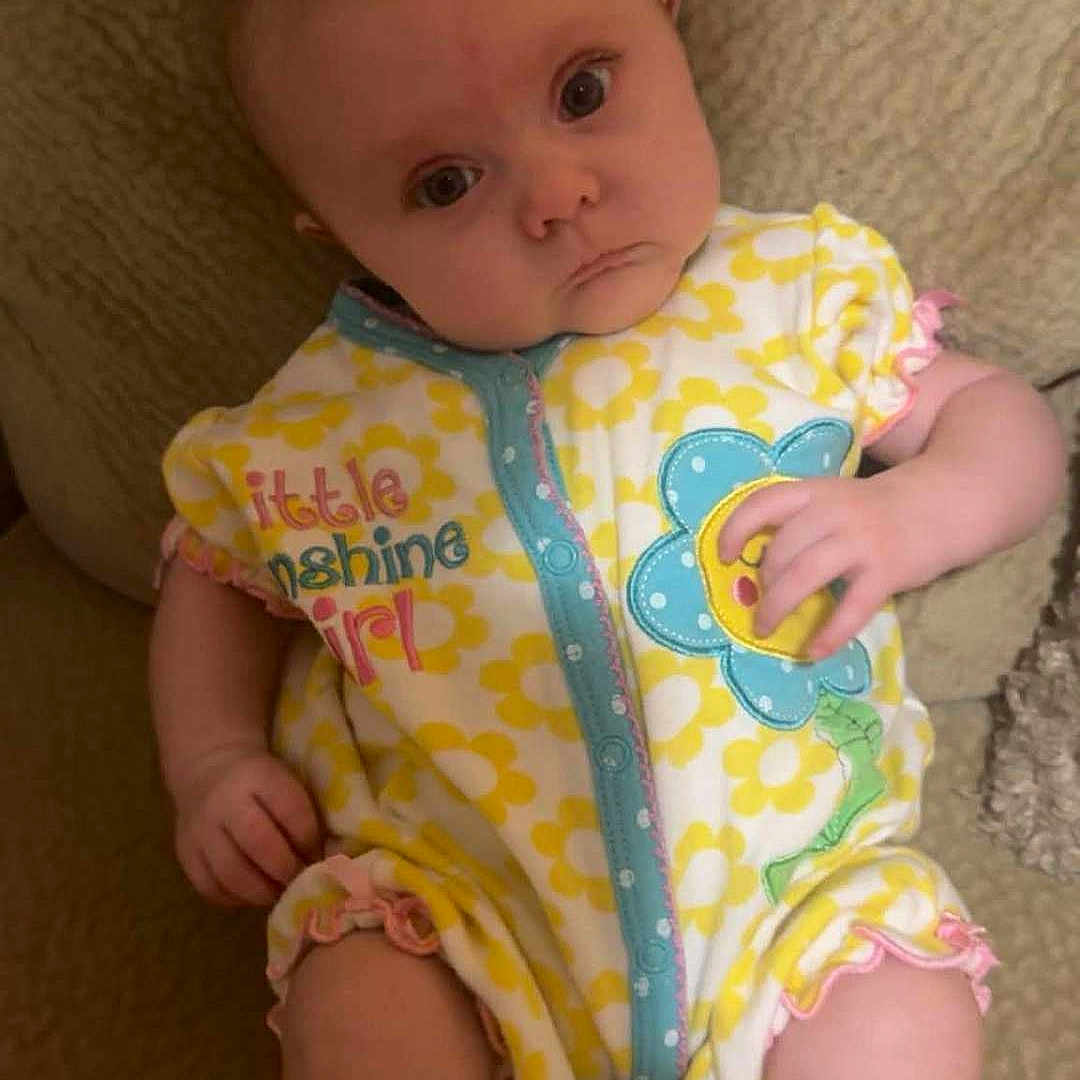 Lillian joined the competition — help win amazing prizes! baby, infant, onesie, yellow, flower, pattern, blanket, soft, cute, child, portrait, clothing, sitting, skin, hand, face, expression, indoor, person, young