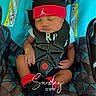 baby, car_seat, headband, red, sleeping, child, infant, socks, black_clothing, safety_harness, patterned_fabric, indoors, peaceful, cute, resting, small_hands, wearing, comfort, seatbelt, nap