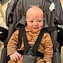 baby, infant, stroller, car_seat, harness, smile, corduroy, brown_outfit, bald_head, wide_eyes, rosy_cheeks, hand, buckle, seat_padding, portrait, closeup, indoor, cute, child, person
