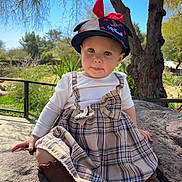 Celina joined the competition — help win amazing prizes! toddler, child, outdoor, rock, hat, dress, plaid, trees, sunlight, nature, cute, portrait, sitting, face, clothing, footwear, earrings, daytime, expression, young_child