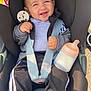 baby, bottle, car_seat, child, clothing, cute, daylight, face, happy, infant, jacket, outside, pants, person, safety, seatbelt, sitting, smiling, socks, young
