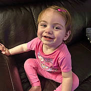 Miley is registered to the contest to win money with this photo: toddler, child, smiling, pink_clothing, hair_clip, couch, leather, indoor, cute, happy, sitting, baby, person, face, foot, hand, casual, portrait, young_child, cozy