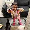 Ziva is registered to the contest to win money with this photo: child, girl, indoor, colorful_clothing, braided_hair, smiling, playful_pose, rug, couch, pillow, slippers, patterned_rug, living_room, wood_floor, furniture, happy, person, portrait, home, casual