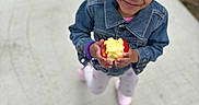 Ziva joined the competition — help win amazing prizes! child, girl, smile, apple, denim_jacket, hair_buns, outdoor, concrete, holding, food, casual_clothing, happy, cute, portrait, person, daylight, walking, footwear, playful, young