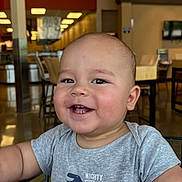 Jaden is registered to the contest to win money with this photo: arm, baby, chair, child, clothing, cute, dinosaur, face, furniture, happy, head, indoor, onesie, person, shopping_cart, skin, smile, store, table, toddler