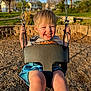 Ivan is registered to the contest to win money with this photo: child, toddler, swing, playground, smile, happy, outdoor, sunlight, blonde_hair, shorts, tshirt, chains, woodchips, grass, trees, residential_area, daytime, fun, park, joy