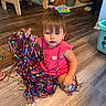 toddler, child, sitting, smiling, pink_outfit, party_streamers, colorful, toy_room, playroom, wooden_floor, plush_dog, toy_cars, baby_toys, indoor, portrait, young_child, festive, birthday, happy, playful