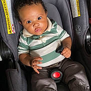 Syreese is registered to the contest to win money with this photo: baby, child, car_seat, seat_belt, clothing, striped_shirt, polo_shirt, pants, socks, indoor, person, infant, seat, safety, curly_hair, black_hair, young_child, cute, wide_eyes, expression