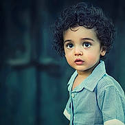 Lol joined the competition — help win amazing prizes! child, toddler, curly_hair, blue_shirt, portrait, face, wide_eyes, expression, innocence, young_child, person, standing, casual_clothing, curious, background_blur, closeup, skin, head, looking_away, indoors