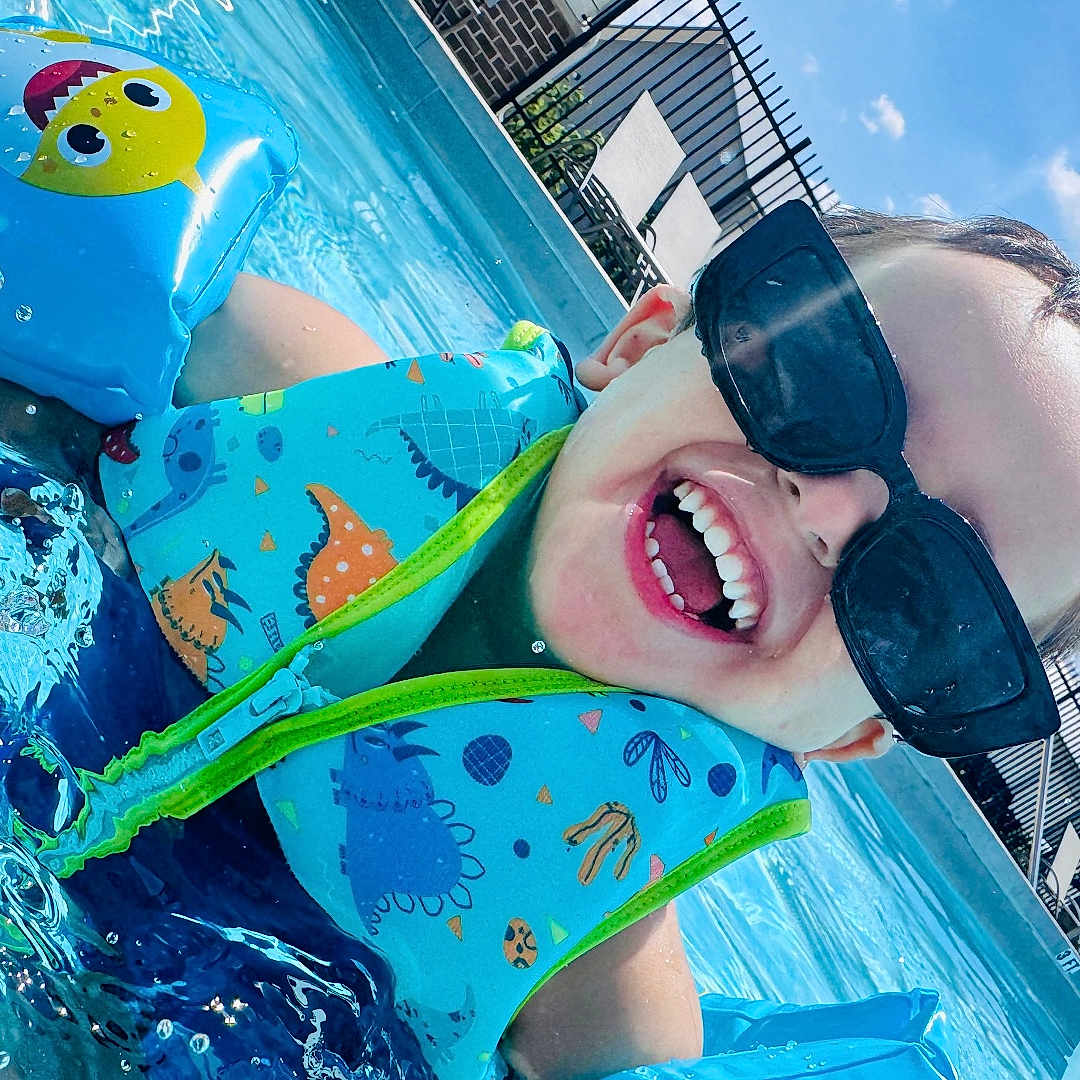 Zael is registered to the contest to win money with this photo: child, pool, water, floaties, sunglasses, happy, smiling, summer, outdoor, blue_sky, clouds, swimming, fun, sunny, splash, vacation, playful, life_jacket, dinosaur_pattern, inflatable
