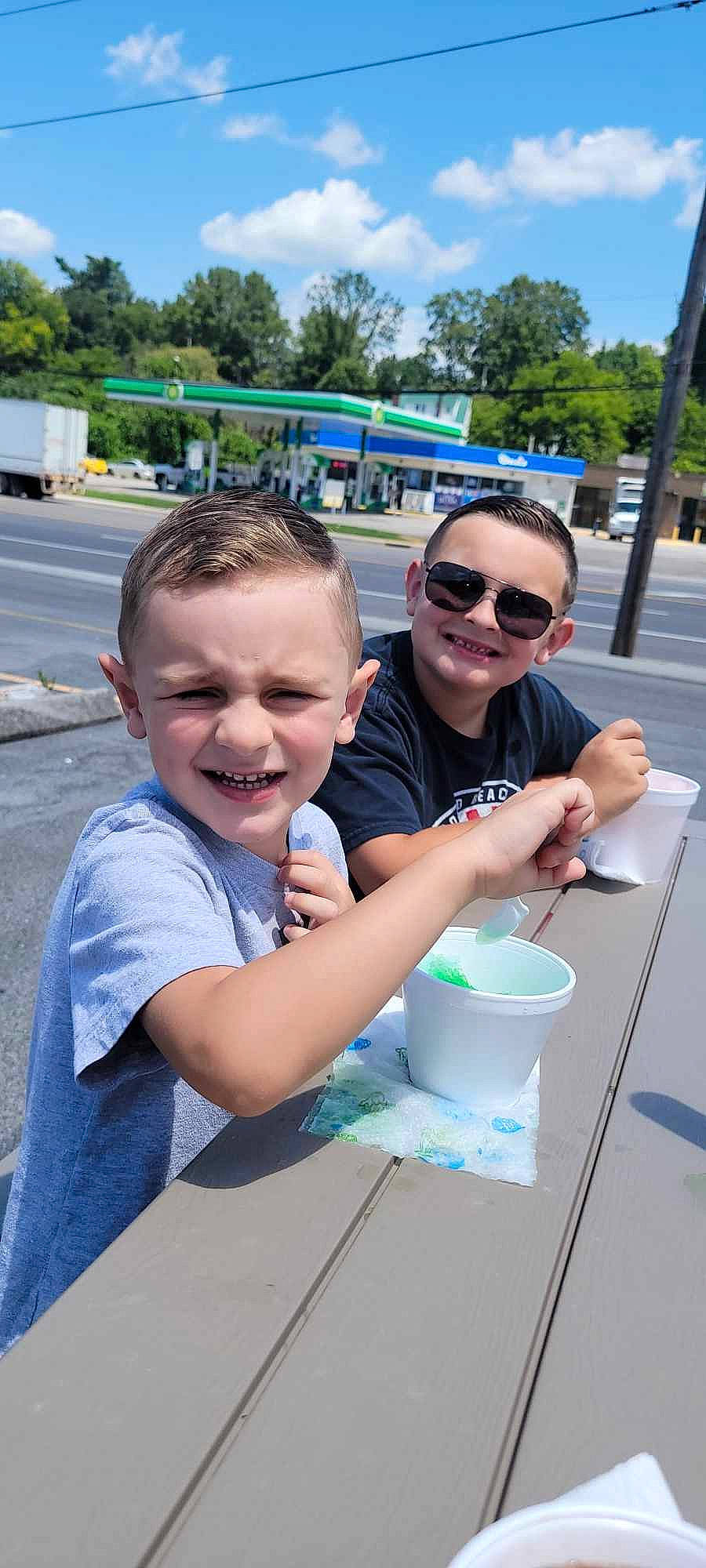 Evan is registered to the contest to win money with this photo: event, eyewear, facial_expression, fun, glasses, goggles, hairstyle, happy, joy, leisure, person, recreation, shorts, sky, smile, sunglasses, t_shirt, table, tableware, toddler