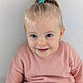toddler, child, smiling, blue_eyes, pink_clothing, hair_tie, pony_tail, sitting, indoor, white_wall, cute, happy, face, young_child, portrait, casual, cozy, innocence, person, clothing