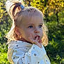 Lia participe au concours pour gagner de l'argent avec cette photo : child, toddler, girl, outdoor, nature, greenery, sunlight, portrait, cute, blue_eyes, hair_tie, jacket, flower_pattern, hand_on_mouth, casual_clothing, daylight, young_child, curious, innocent, garden