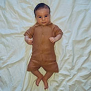 Télio participe au concours pour gagner de l'argent avec cette photo : baby, infant, child, clothing, brown_outfit, lying_down, white_sheet, bed, wrinkles, face, skin, hands, feet, shorts, button_up, portrait, indoor, looking_at_camera, cute, young