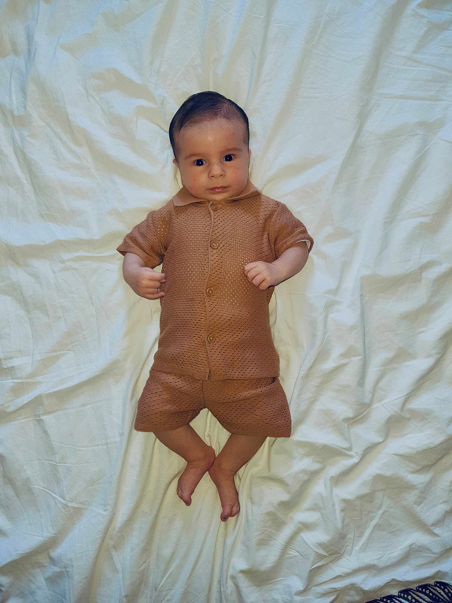 Télio participe au concours pour gagner de l'argent avec cette photo : baby, infant, child, clothing, brown_outfit, lying_down, white_sheet, bed, wrinkles, face, skin, hands, feet, shorts, button_up, portrait, indoor, looking_at_camera, cute, young