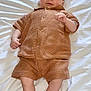 Télio participe au concours pour gagner de l'argent avec cette photo : baby, infant, child, knitwear, brown_clothing, lying_down, bed_sheet, portrait, cute, young, person, skin, small_hands, small_feet, shorts, shirt, casual, indoors, relaxed, looking_at_camera