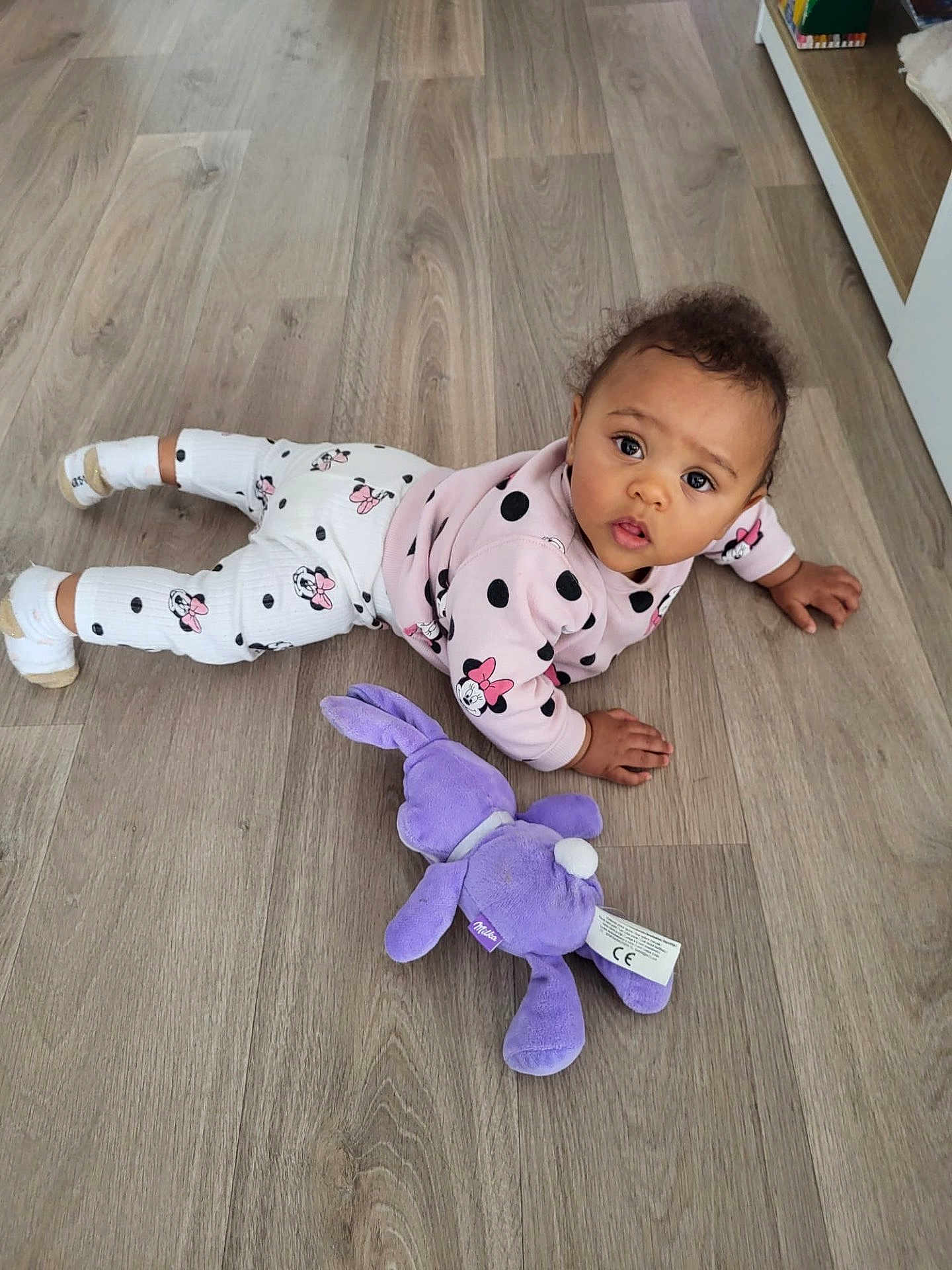 Janelle participe au concours pour gagner de l'argent avec cette photo : baby, child, floor, plush_toy, toy, pajamas, minnie_mouse, pink_clothing, white_clothing, polka_dots, curly_hair, indoor, wooden_floor, socks, cute, looking_up, infant, crawling, playtime, soft_toy