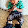 Zayden is registered to the contest to win money with this photo: toddler, child, smiling, green_shirt, jeans, sneakers, black_shoes, blue_soles, couch, indoor, happy, hands_clasped, seated, young_child, casual_clothing, portrait, cute, baby, fashion, footwear