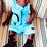 baby, black_shoes, black_skin, blue_outfit, boy, casual_clothing, child, comfortable, curious, fashion, indoor, looking_sideways, portrait, short_hair, sitting, sneakers, sock, striped_couch, stylish, young_child
