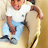 toddler, child, smiling, happy, indoor, chair, white_shirt, blue_jeans, ripped_jeans, socks, furniture, floor, wall, golden_accent, cute, portrait, seated, young_child, casual_clothing, joyful