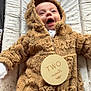 baby, infant, onesie, fluffy_clothing, teddy_bear, plaque, milestone, changing_pad, patterned_background, smiling, cute, happy, lying_down, indoor, child, face, head, person, warm_clothing, newborn