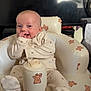 baby, infant, smiling, sitting, indoors, pajamas, inflatable_chair, bear_pattern, cozy, cute, child, furniture, playful, happy, person, home, relaxed, young_child, soft_lighting, comfort