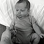 baby, infant, hand, tattoo, pillow, clothing, sitting, monochrome, black_and_white, person, skin, arm, face, expression, background, soft_surface, holding, support, newborn, cute