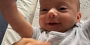 Mateo joined the competition — help win amazing prizes! baby, infant, hand, smile, person, clothing, onesie, bed, changing_pad, pattern, playful, happy, skin, face, arm, interaction, indoor, closeup, joyful, candid