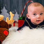 baby, infant, plush_toy, reindeer, holiday, christmas, decorations, red_nose, fur, blue_clothing, cute, indoor, child, face, toy, festive, winter, background_blur, soft_texture, smiling