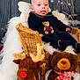 baby, infant, wicker_chair, plush_toys, reindeer, bear, winter_theme, holiday_decor, blue_outfit, teddy_bear_design, fluffy_blanket, cute_expression, tongue_out, indoor, portrait, child, smiling, festive, decorations, soft_toys