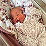 newborn, baby, infant, floral_onesie, blanket, patterned_blanket, resting, sleepy, cozy, indoors, cute, child, soft_light, bed, pink, white, small_hand, face, portrait, peaceful