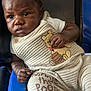 baby, black, blue, child, clothing, cozy, cute, expression, face, furniture, hand, indoors, infant, looking_away, onesie, person, portrait, seated, winnie_the_pooh, young