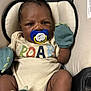 Robert is registered to the contest to win money with this photo: apparel, baby, beige, blue, child, closeup, clothing, comfort, cushion, cute, expression, face, indoor, infant, mittens, onesie, pacifier, person, seat, skin