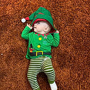 Nikodem is registered to the contest to win money with this photo: baby, carpet, child, christmas, cozy, cute, elf_hat, face, festive, green_clothing, holiday_outfit, indoor, infant, lying_down, portrait, smiling, soft_texture, striped_pants, white_socks, young_child