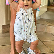 Jacob is registered to the contest to win money with this photo: baby, child, infant, white_romper, sneakers, holding_hands, smiling, indoor, tile_floor, cute, chubby_cheeks, walking, support, person, footwear, happy, young_child, family, parent, helping