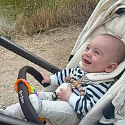 Emile a rejoint le concours — aidez-le/la à gagner de superbes lots ! baby, smiling, stroller, outdoor, grass, water, toy, clothing, person, infant, happy, nature, seatbelt, footwear, handlebar, path, daylight, headwear, cute, child
