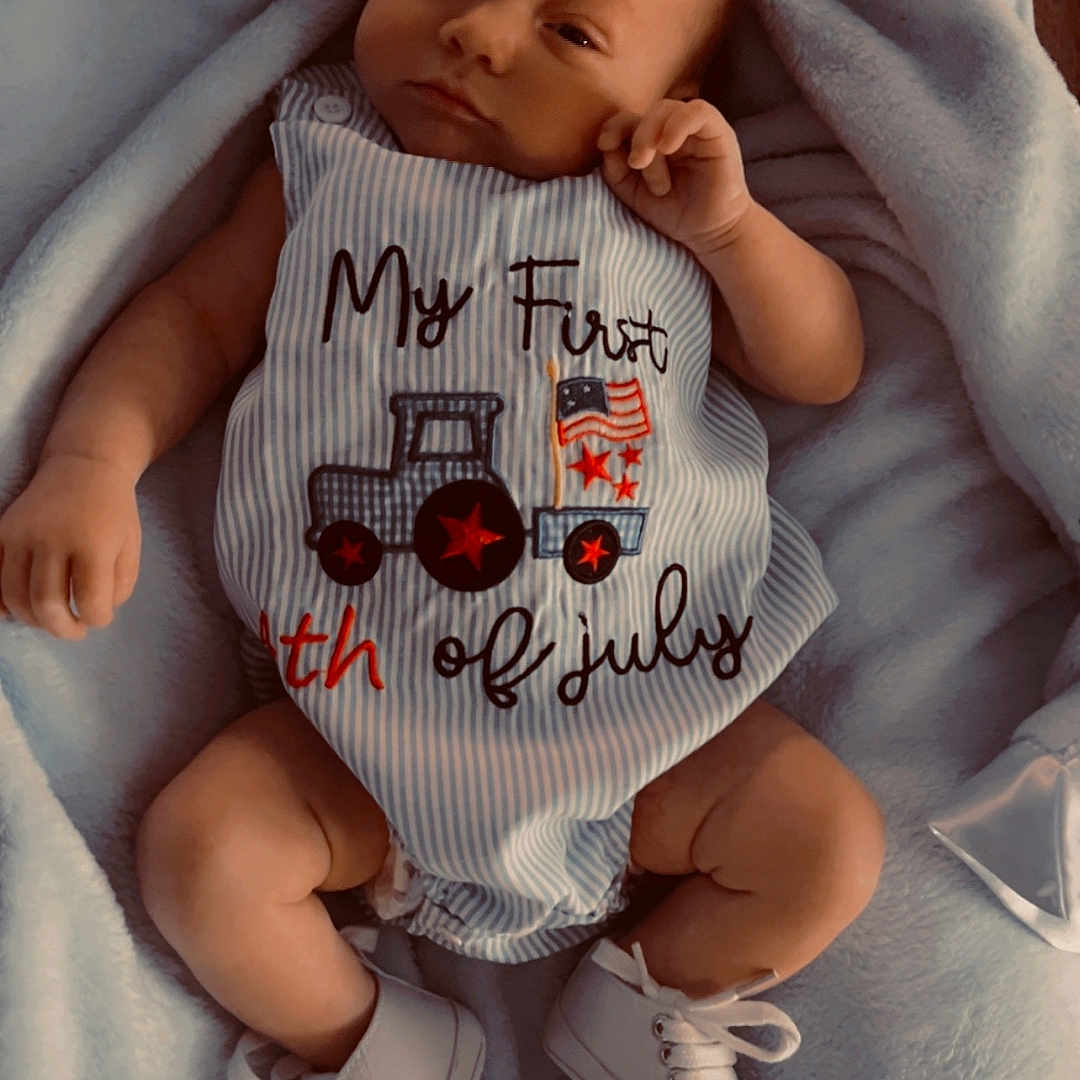 Jasper is registered to the contest to win money with this photo: baby, infant, blanket, clothing, shoes, blue, striped, text, floor, wood, cute, young_child, portrait, laying_down, small_shoes, soft_texture, comfortable, indoors, celebration, holiday_outfit