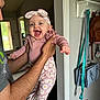 adult_arm, baby, child, cute, daisy_pattern, door, handbag, happy, headband, holding, home_interior, indoor, joyful, laughing, person, pink_clothing, portrait, smiling, socks, wall_hooks