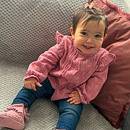 éline participe au concours pour gagner de l'argent avec cette photo : baby, child, smiling, pink_clothing, jeans, booties, couch, pillow, indoor, happy, cute, hair_bow, portrait, seated, young_child, furniture, cozy, face, person, home