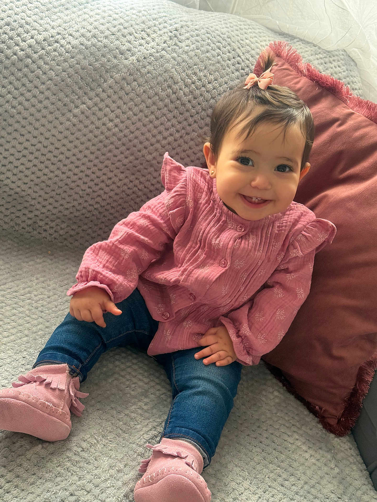 éline participe au concours pour gagner de l'argent avec cette photo : baby, child, smiling, pink_clothing, jeans, booties, couch, pillow, indoor, happy, cute, hair_bow, portrait, seated, young_child, furniture, cozy, face, person, home