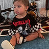 baby, black_clothing, carpet, checkered_pattern, child, curious, cute, drum_set, earrings, floor, indoor, metallica, musical_instruments, person, rock_music, short_hair, sitting, sneakers, toddler, tshirt