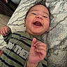 Kaziel is registered to the contest to win money with this photo: baby, infant, child, smiling, laughing, portrait, close_up, lying_down, blanket, bed, indoors, green_clothing, striped_clothing, long_sleeves, dark_hair, happy, hands, fists, cozy, photography