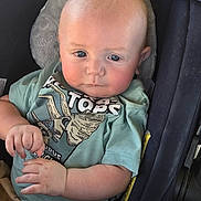 Aulcard is registered to the contest to win money with this photo: baby, infant, child, portrait, car_seat, seated, wide_eyes, blue_eyes, serious_expression, fair_skin, mint_green_shirt, graphic_shirt, blanket, hands, arms, indoor, close_up, photography, safe, vehicle