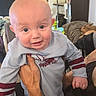 Aulcard is registered to the contest to win money with this photo: baby, infant, child, portrait, smiling, wide_eyed, indoors, being_held, adult_hand, gray_shirt, striped_sleeves, clothing, cat, pet, couch, living_room, bookshelf, furniture, close_up, family_photo