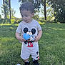 toddler, child, mickey_mouse, outdoor, grass, trees, daylight, shirt, shorts, black_shoes, blue_bottle_lids, curious, standing, nature, sunlight, clothing, person, footwear, playtime, summer