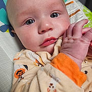 Noah is registered to the contest to win money with this photo: baby, infant, child, portrait, face, eyes, hands, looking_at_camera, wide_eyed, pajamas, clothing, orange, patterned, blanket, baby_seat, cushion, indoors, close_up, photography, adorable