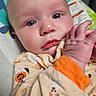 baby, infant, child, portrait, face, eyes, hands, looking_at_camera, wide_eyed, pajamas, clothing, orange, patterned, blanket, baby_seat, cushion, indoors, close_up, photography, adorable